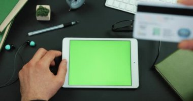 Adam yeşil ekran ve yeşil ekran bir masada kredi kartından türleri bilgi ile bir tablet tutar