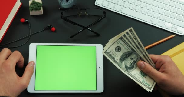 Man holds hundreds of dollars in his arm and then types something on the green screen of a tablet — Stock Video