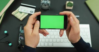 Adam yeşil ekran siyah bir smartphone bir çalışma tablo üzerinde tutan ve üzerine bir şey verilirse