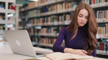 Kız öğrenci kitap ve Kütüphane masada oturan bir dizüstü bilgisayar ile çalışır