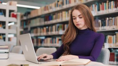 Kız öğrenci kitap ve Kütüphane masada oturan bir dizüstü bilgisayar ile çalışır