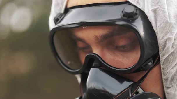 Hombre con máscara de gas y traje de bio-peligro mira hacia abajo tomando notas en su tableta — Vídeos de Stock