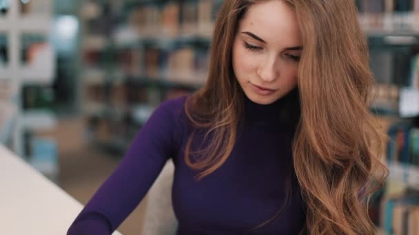 Meisje schrijft iets uit een boek zitten aan de tafel in een bibliotheek — Stockvideo