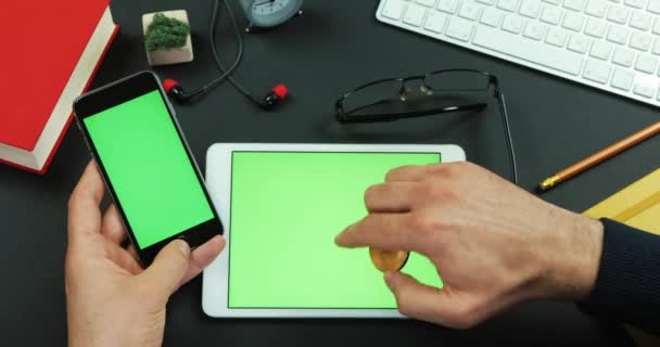 Uomo tiene smartphone con schermo verde su un tavolo con schermo verde e un Bitcoin nella mano destra — Video Stock