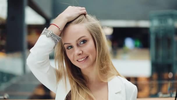 Sorrindo jovem mulher loira parece encantador consertar seu cabelo para uma câmera — Vídeo de Stock
