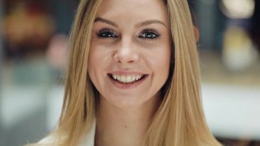 Gülümseyen genç sarışın kadın saçlarını bir kamera için sabitleme büyüleyici görünüyor