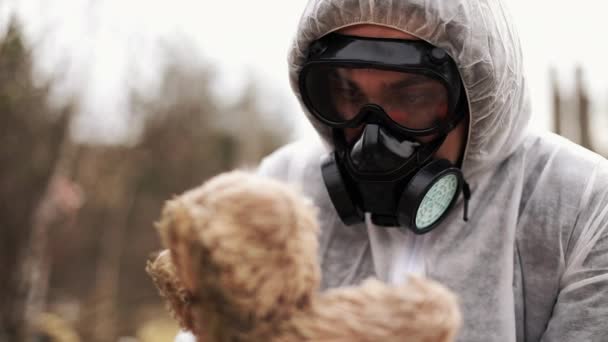 Seorang pria dalam pakaian bio-hazard dan masker gas membawa mainan di lengannya — Stok Video