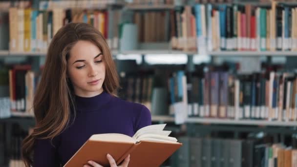 Doordachte jonge vrouwelijke student leest een boek staan in de bibliotheek — Stockvideo