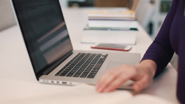 Estudante trabalha com livros e um laptop sentado à mesa na biblioteca — Vídeo de Stock