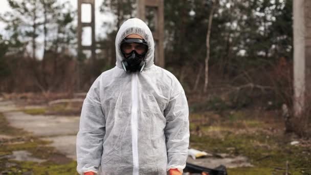 Man in bio-hazard suit and gas masks stands behind the stripe on the territory full of waste — Stock Video