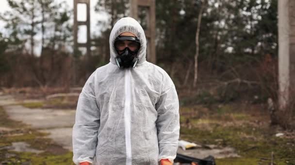 Man in bio hazard suit and gas masks stands behind the stripe on the territory full of waste 193425250