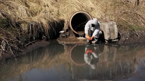 Man in bio-hazard suit and gas mask checks the pollution of the water outside — Stock Video