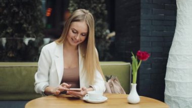 Sevimli sarışın kadın bir şey kafede masada oturan onun smartphone içinde okur