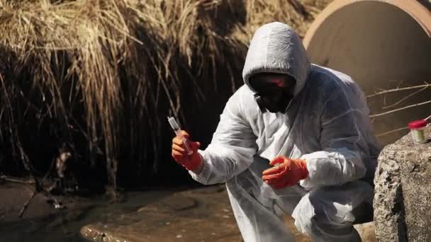 L'homme en costume bio-danger et masque à gaz vérifie la pollution de l'eau à l'extérieur — Video