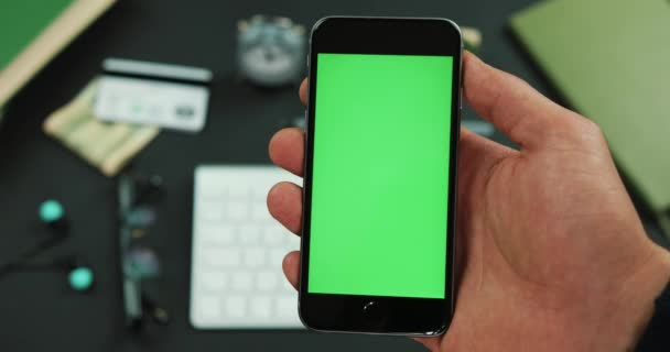 El hombre sostiene el teléfono inteligente con pantalla verde sobre una mesa de trabajo — Vídeo de stock