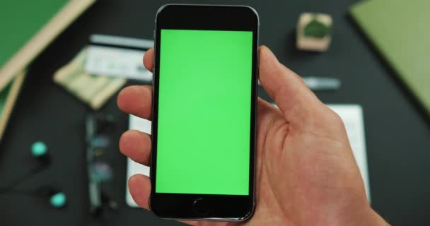 Uomo tiene uno smartphone nero con schermo verde su un tavolo da lavoro — Video Stock
