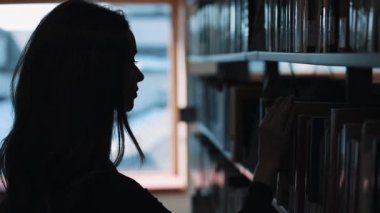 Daha önce bir raf kütüphanede kitap bakarak bir kız silüeti