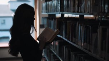 Daha önce bir raf kütüphanede kitap bakarak bir kız silüeti