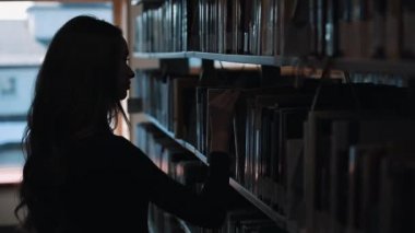 Daha önce bir raf kütüphanede kitap bakarak bir kız silüeti