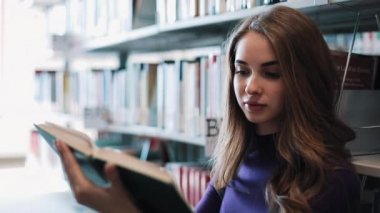 Düşünceli genç kız öğrenci Kitaplığı'nda bekleyen bir kitap okur