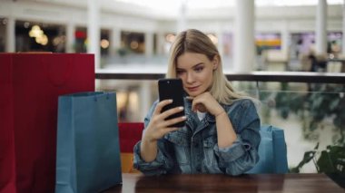 Güzel sarışın kız selfie alışveriş torbaları ile kafede oturan telefonu alır