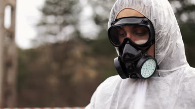 Gaz maskesi ve biyo-tehlike takım elbiseli adam onun tablet üzerinde notlar alarak görünüyor