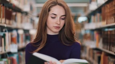 Düşünceli genç kız öğrenci Kitaplığı'nda bekleyen bir kitap okur