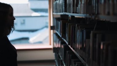 Daha önce bir raf kütüphanede kitap bakarak bir kız silüeti
