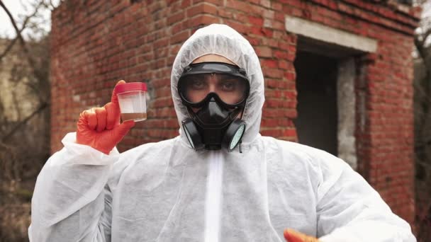 L'homme en costume bio-danger et masque à gaz montre de l'eau polluée et des signes non verbaux — Video