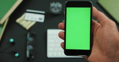 Adam yeşil ekran siyah bir smartphone bir çalışma tablosu üzerinde tutar.