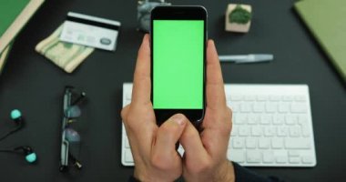Adam yeşil ekran siyah bir smartphone bir çalışma tablo üzerinde tutan ve üzerine bir şey verilirse