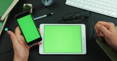 Adam yeşil ekran içeren bir tablo üzerinde yeşil ekran ile akıllı telefon tutar ve üzerine bir şeyler musluklar