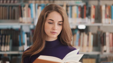 Düşünceli genç kız öğrenci Kitaplığı'nda bekleyen bir kitap okur