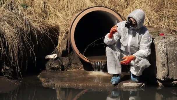 Man in pak en gas masker van de bio-gevaar controleert de vervuiling van het water buiten — Stockvideo