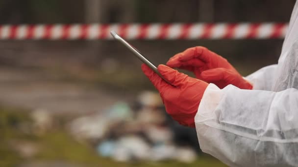 Mann in Biogefährdungsanzug und Gasmaske macht sich Notizen in seinem Tablet, das auf dem verseuchten Land steht — Stockvideo