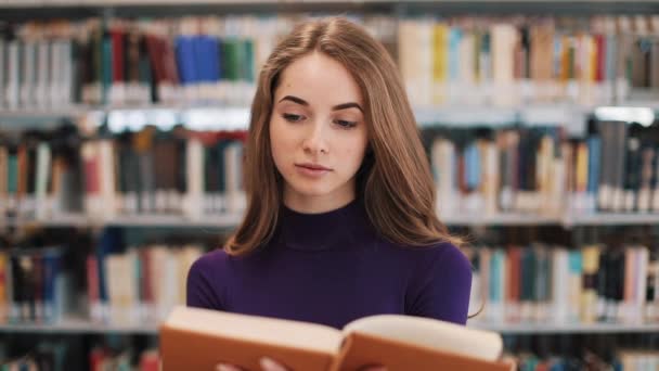 Nachdenkliche junge Studentin liest in der Bibliothek ein Buch — Stockvideo