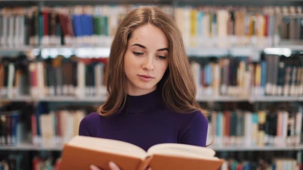 Στοχαστικοί νέοι φοιτήτριας διαβάζει ένα βιβλίο στέκεται στη βιβλιοθήκη — Αρχείο Βίντεο