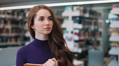 Kütüphanede bir kitapla düşünceli kız duruyor