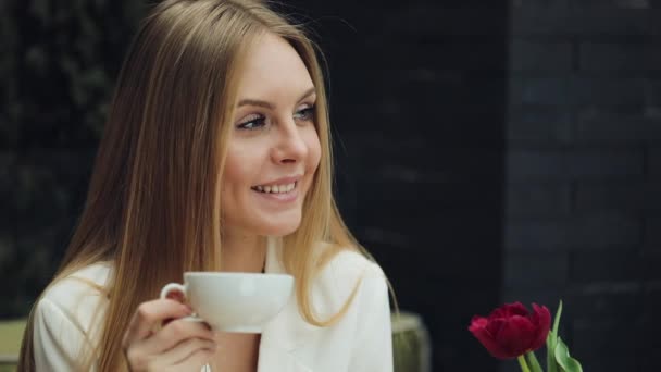 Schattige jonge vrouw drinkt haar koffie zitten in het cafe — Stockvideo