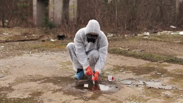 Человек в защитном костюме и противогазах забирает воду и землю для анализа — стоковое видео