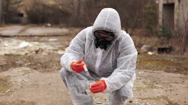 Hombre en traje de bio-peligro y máscaras de gas toma agua y tierra para el análisis — Vídeos de Stock