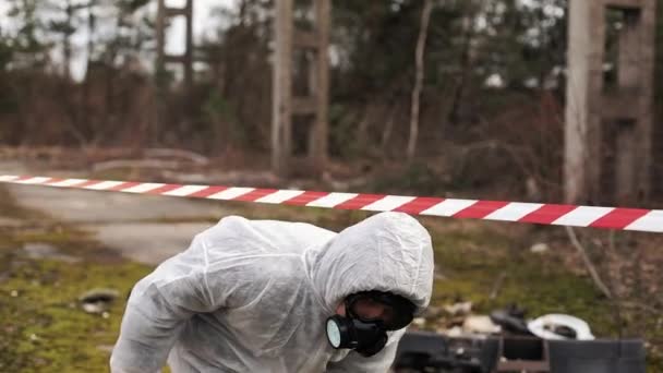 Man in bio-hazard suit and gas mask walks to the stipe on the land full of waste — Stock Video