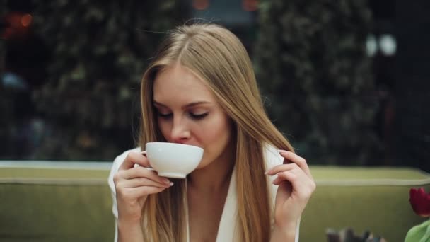 Schattige jonge vrouw drinkt haar koffie zitten in het cafe — Stockvideo