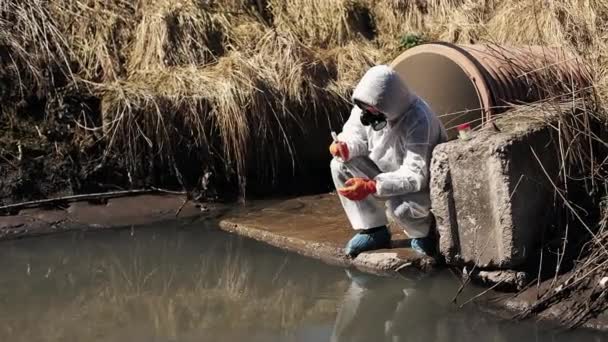 Man in bio-hazard suit and gas mask checks the pollution of the water outside — Stock Video