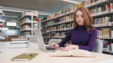 Kız öğrenci kitap ve Kütüphane masada oturan bir dizüstü bilgisayar ile çalışır