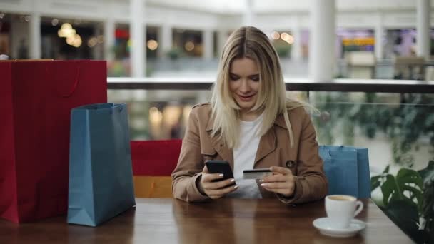 Meisje wirtes een aantal creditcard zitten met boodschappentassen in het café — Stockvideo