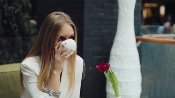 Imádnivaló, fiatal nő issza a kávéját, a kávéházban ült — Stock videók