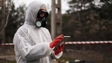 Biyo-tehlike takım elbise ve gaz maskesi alır onun tablet duran kirli karada notlarda erkekte