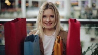 Mutlu sarışın kadın renkli alışveriş torbaları alışveriş merkezinin arkasında duruyor