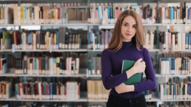 Kız öğrenci gülümseyen bir kitap an burada raflar kütüphanede tutar